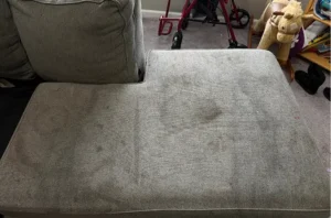 Dark pet stains soaked into a gray sofa seat before upholstery cleaning in Atlanta, GA by the Couch Steamers team