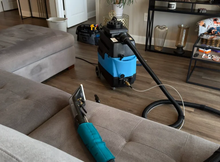 In-home couch cleaning setup with professional extraction machine, hoses, and upholstery tool prepared for deep sofa cleaning service.