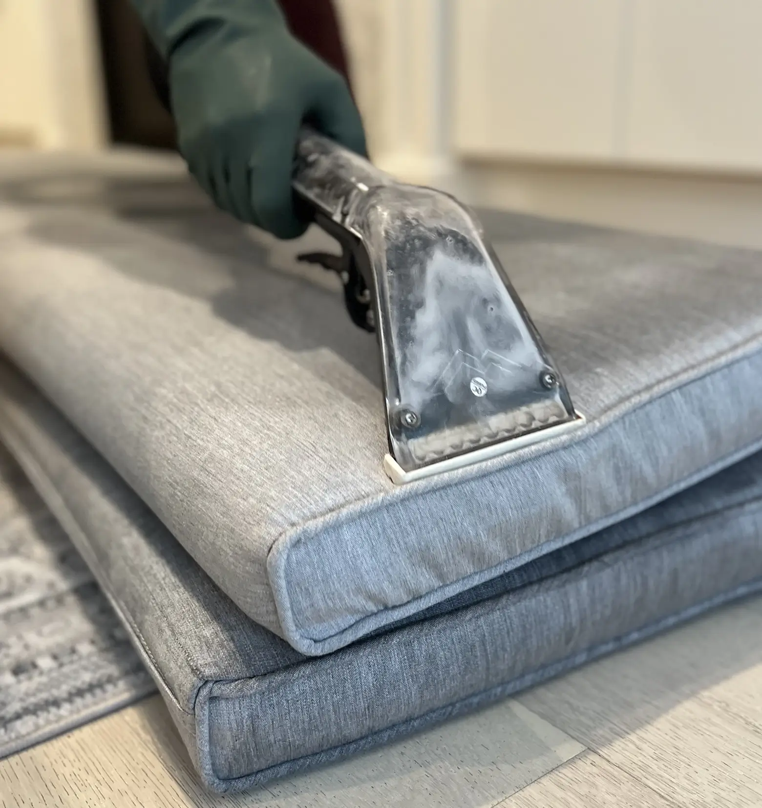 Close-up of professional sofa cleaning with an upholstery extraction wand cleaning a gray fabric seat cushion. Deep fabric cleaning process for dirt removal, stain treatment support, and freshening upholstered furniture.