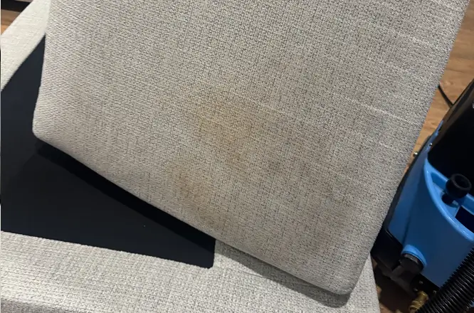 Close-up of a fabric couch cushion with visible surface soiling before professional upholstery deep cleaning.