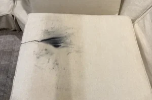 Linen ottoman with dark ink stain before upholstery cleaning in Raleigh, NC by the Couch Steamers team