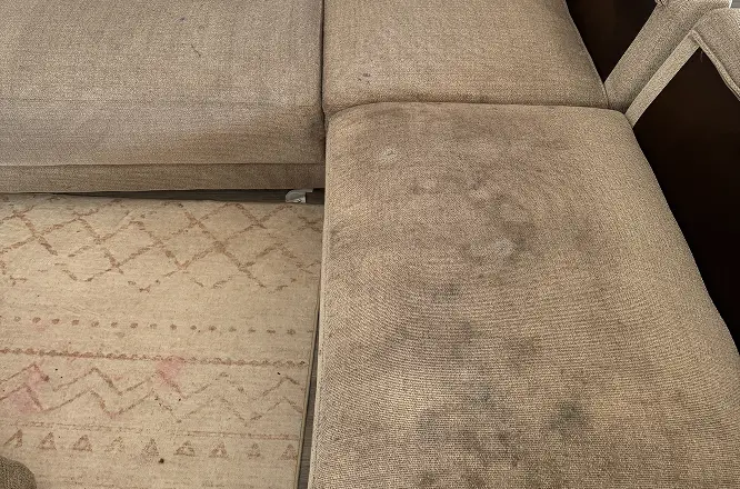 Sectional upholstery surfaces with old dark stains and embedded soiling before professional upholstery cleaning in Raleigh, NC.