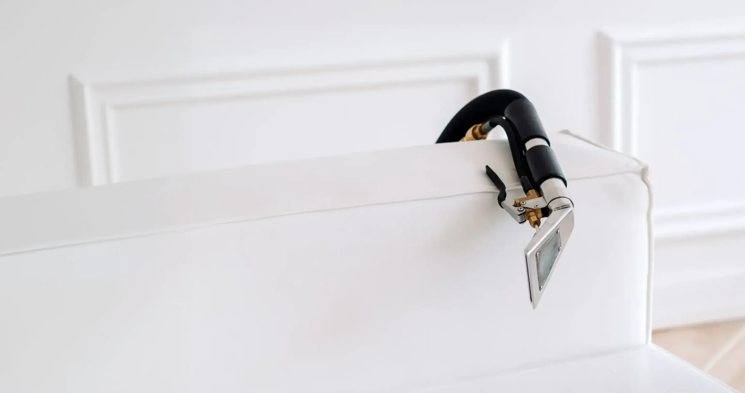 Professional upholstery cleaning service hero image showing a white sofa being cleaned with a professional upholstery extraction tool. Clean modern interior background photo for sofa cleaning and upholstery cleaning website homepage.