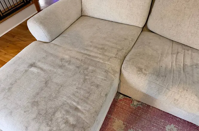 Light sectional couch chaise with visible dark stains and heavy soiling before deep upholstery stain removal.