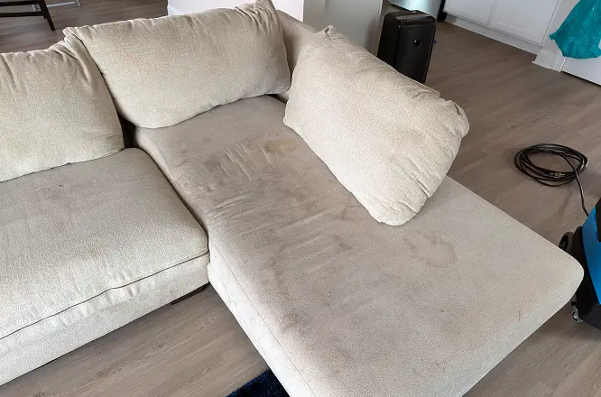 Light sectional couch with visible pet stains and soiled seating area before upholstery cleaning in Atlanta, GA.