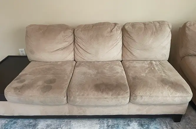Fabric sofa with heavy dirt buildup and darkened seat cushions before professional upholstery deep cleaning.