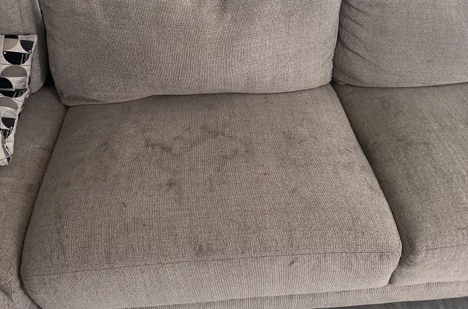 Fabric couch seat cushion with visible spill stains and liquid marks before professional upholstery cleaning.