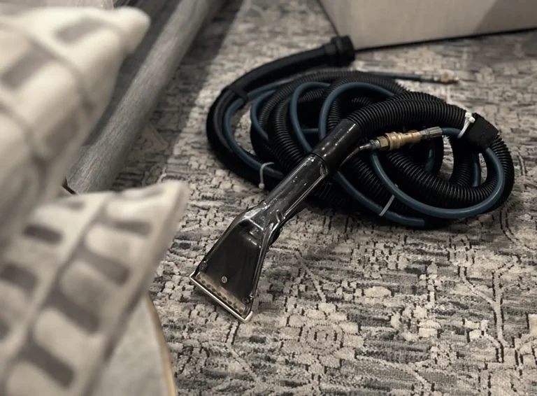 Close-up of a professional upholstery extraction tool cleaning a fabric surface near a patterned rug during deep couch cleaning service.