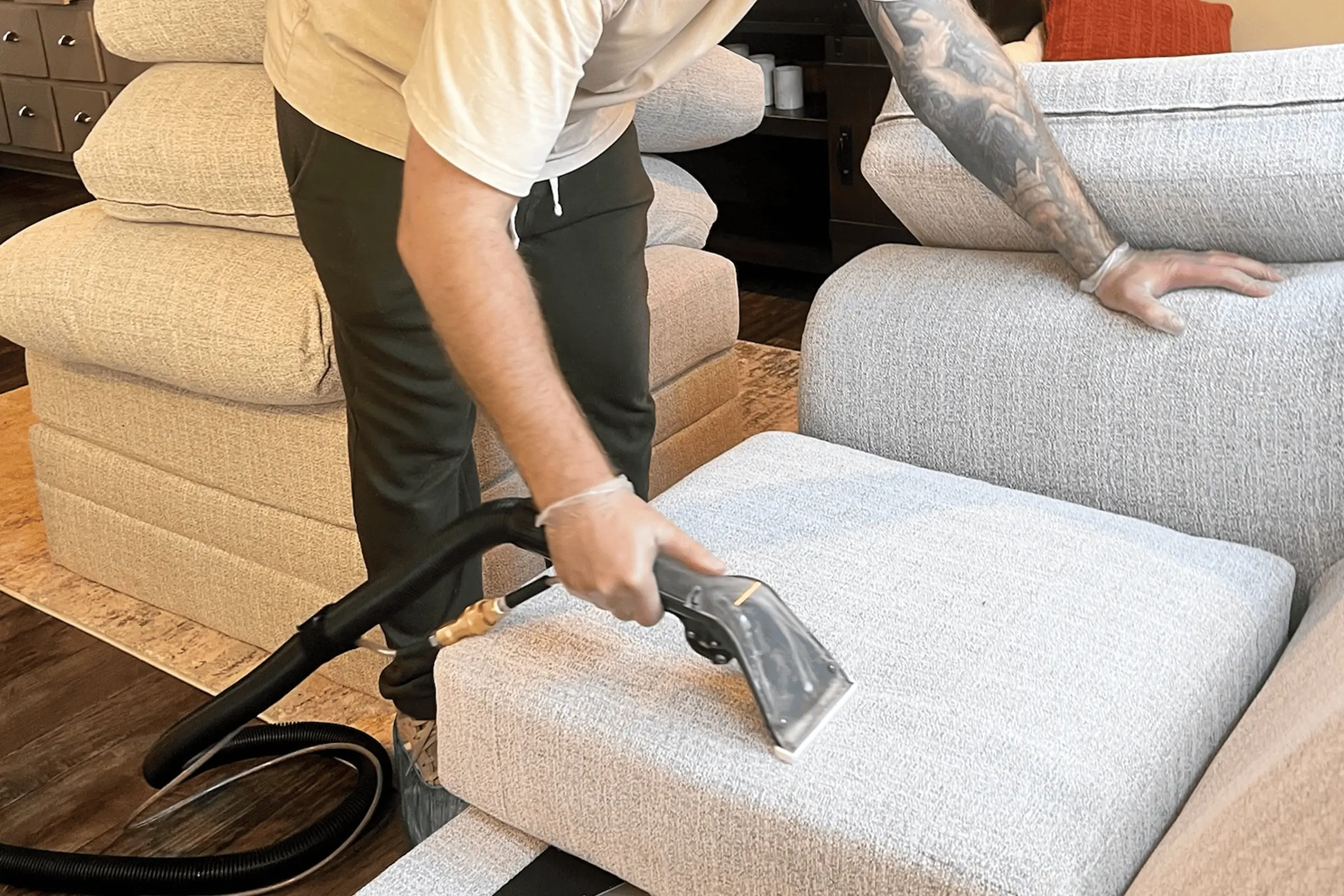 Professional technician performing steam couch cleaning service on a light gray sofa cushion using extraction equipment