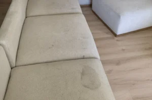 Beige sofa seat with a dark water spot before deep stain upholstery cleaning in Charlotte, NC by Couch Steamers.