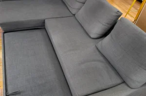 Gray sectional with dull, dusty fabric and flat cushions before a general refresh sofa cleaning by our team.