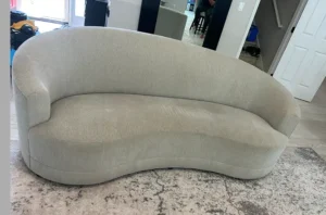 Beige curved sofa with pet stains and dull fabric before upholstery cleaning in Denver, CO by our trained technicians.