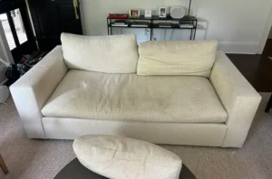 Cream fabric sofa with pet stains and dark spots before upholstery cleaning in Dallas, TX by our couch cleaning services team.