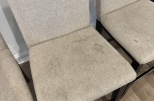 Light fabric counter stools before chair cleaning, with dark marks and dingy spots across the seat cushions.