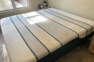 Striped mattress before mattress cleaning, with old yellow stains and dull worn spots across the top surface.