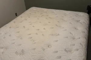 White quilted mattress before mattress deep cleaning, with deep set-in stains spread across the whole top.