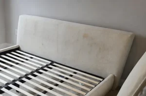 Upholstered white headboard before mattress stain removal, with dark pet stains soaked into the fabric.