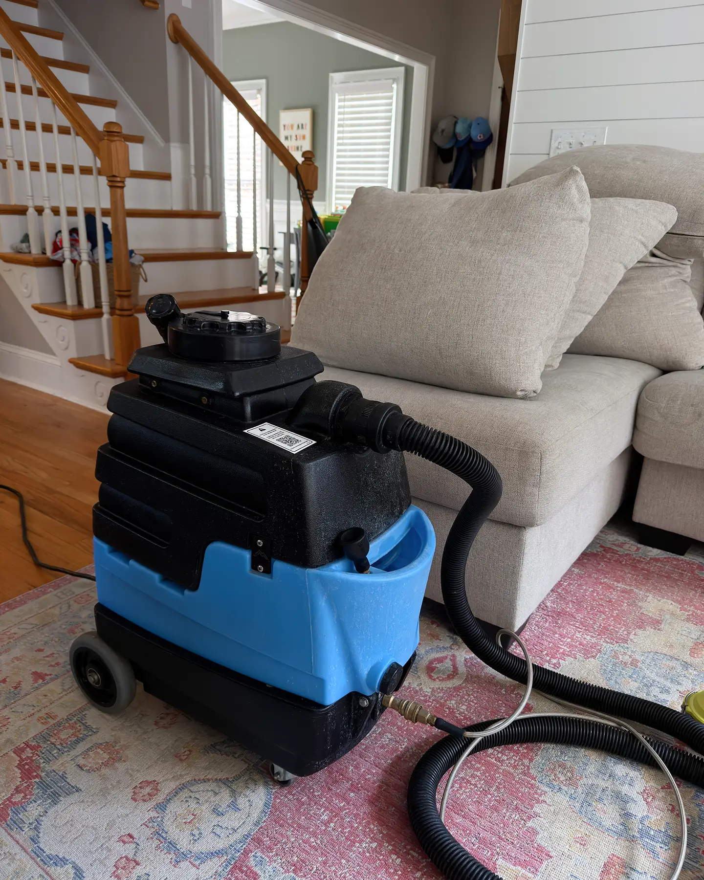 Couch Steamers extractor on a patterned area rug beside a gray sofa. Professional rug cleaning for a fresh, spotless home.