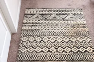 Black and white patterned rug before professional rug cleaning, with dull grime dimming the bold design.