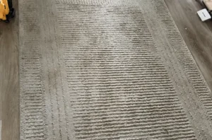 Beige textured rug before rug stain removal, darkened by dog urine stains and heavy soil across the surface.