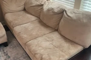 Tan microfiber sofa before sofa cleaning, showing dark pet stains and matted fabric on the seat cushions.