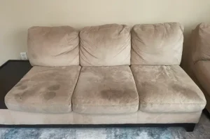 Tan three seat sofa before sofa deep cleaning, with built up dirt and body oils darkening every cushion.