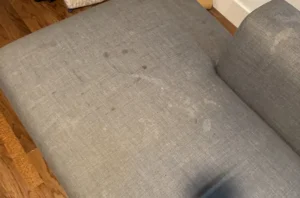Gray sectional before steam couch cleaning, with a dark ink like stain marking the corner of the seat cushion.