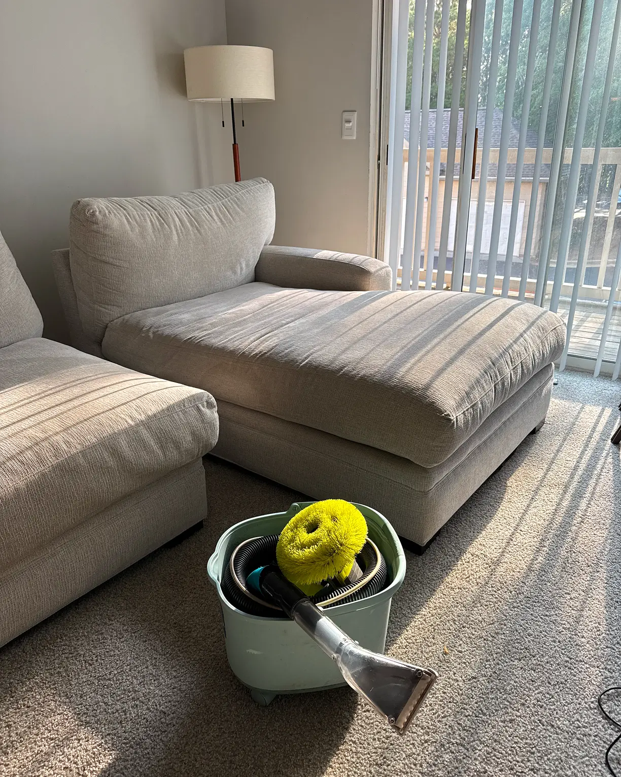 Upholstery wand brush and bucket beside a beige sectional after an upholstery clean in a sunny Dallas home